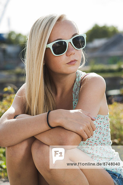 Portrait of teenage girl sitting outdoors  wearing sunglasses and looking to the side  Germany