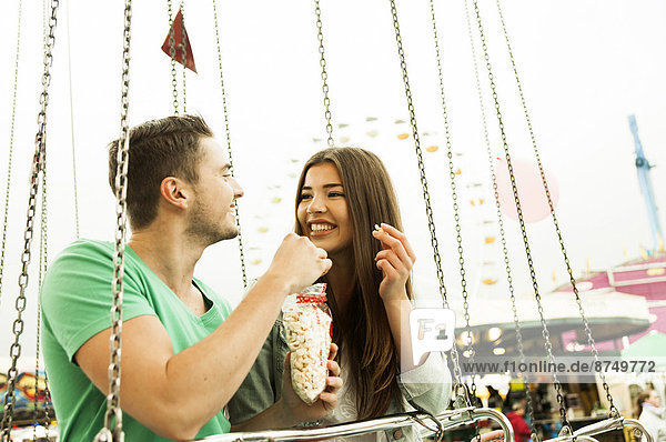Young couple sitting on amusement park ride eating popcorn  Germany