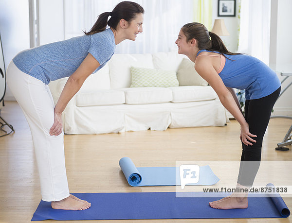 Caucasian mother and daughter practicing yoga in living room