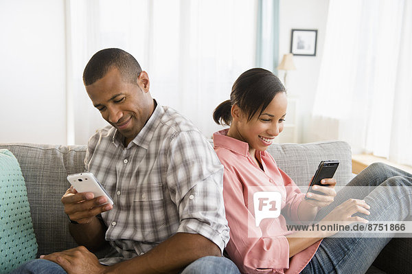 Couple using cell phones back to back on sofa
