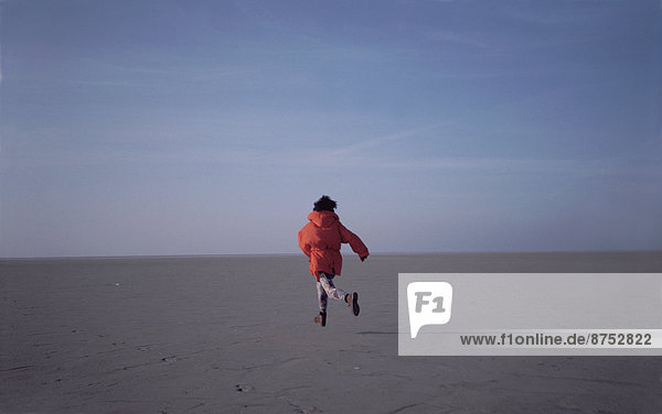 Woman running on sand flats rear view
