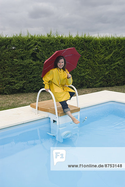 woman in rainwear tipping toe into swimming pool