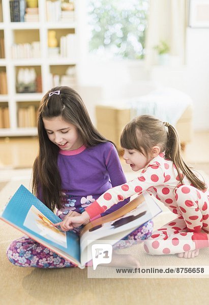 Two sisters (4-5 8-9) reading picture book