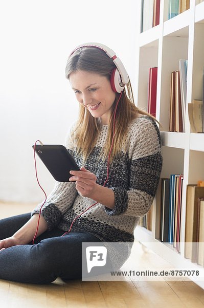 Young woman sitting on floor and listening to music on digital tablet