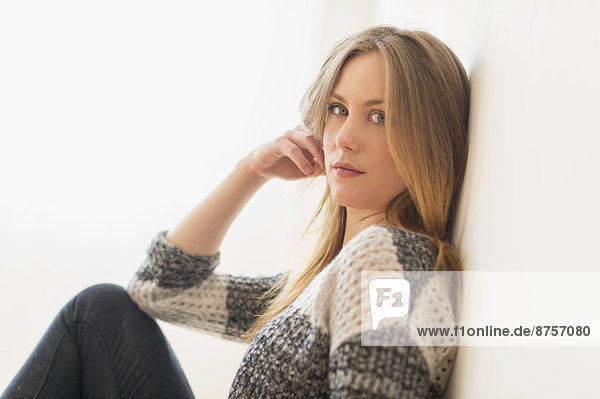 Portrait of attractive young woman sitting by wall