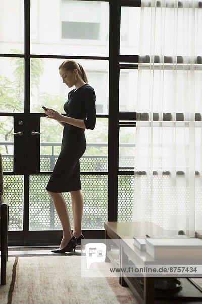 Young businesswoman standing inside and text messaging