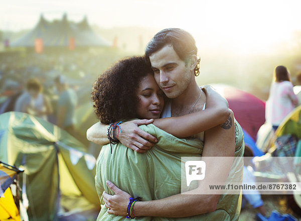 Couple in sleeping bag hugging outside tents at music festival