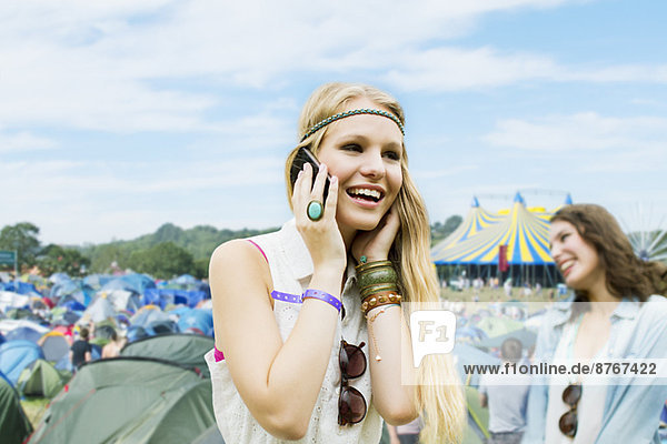 Frau spricht auf dem Handy vor den Zelten beim Musikfestival