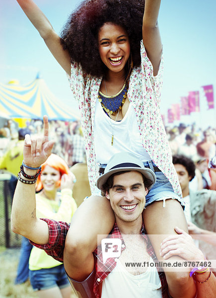 Porträt eines Mannes mit begeisterter Frau auf den Schultern beim Musikfestival