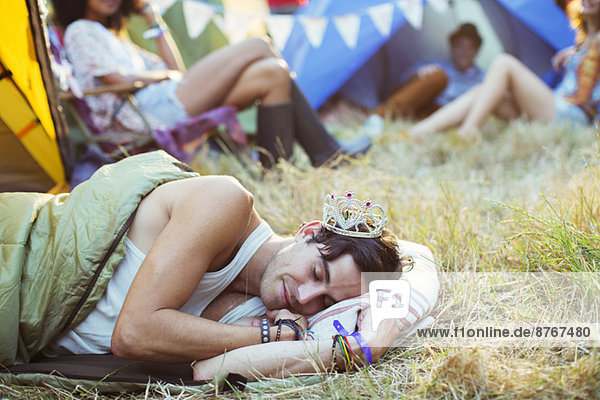 Mann im Diadem schlafend im Schlafsack vor den Zelten beim Musikfestival