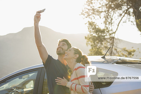 Glückliches Paar beim Selbstporträt mit Fotohandy außerhalb des Autos