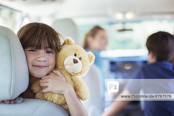Porträt des glücklichen Mädchens mit Teddybär auf dem Rücksitz des Autos