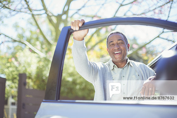 Porträt eines glücklichen älteren Mannes  der sich an die Autotür lehnt.