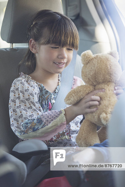Mädchen mit Teddybär auf dem Rücksitz des Autos