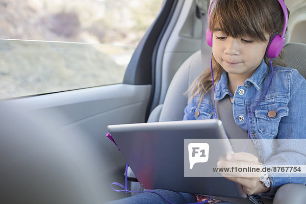 Mädchen mit Kopfhörer mit digitalem Tablett auf dem Rücksitz des Autos