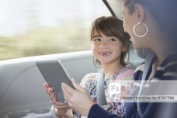 Happy mother and daughter using digital tablet in back seat of car
