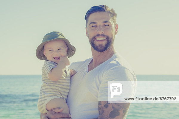 Porträt von Vater und Sohn lächelnd am sonnigen Strand