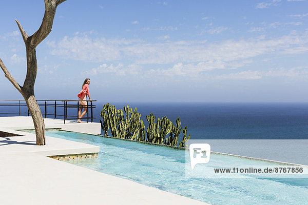 Frau steht auf dem Balkon am Pool mit Blick auf den Ozean