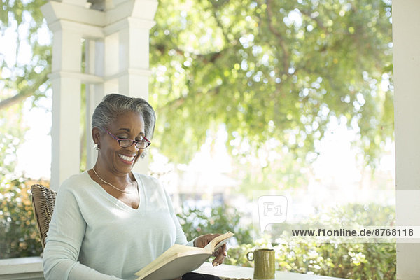 Glückliche Seniorin beim Lesen auf der Veranda