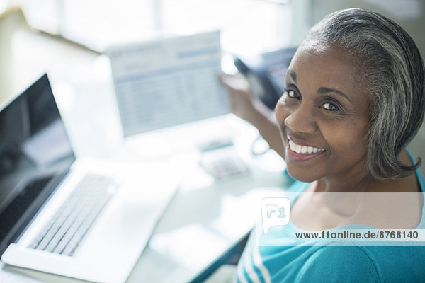 Porträt einer lächelnden Frau  die Rechnungen am Laptop bezahlt