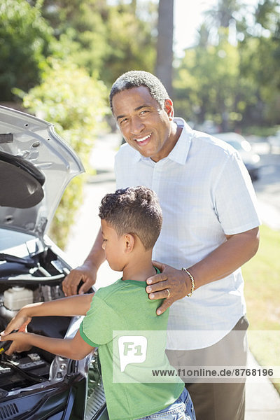 Portrait of smiling grandfather working on car engine with grandson