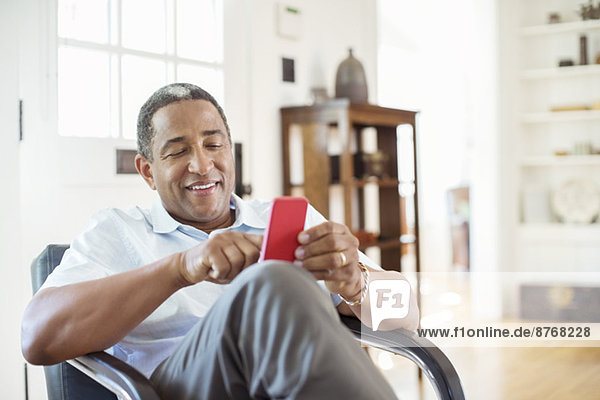 Senior Mann SMS mit Handy im Wohnzimmer