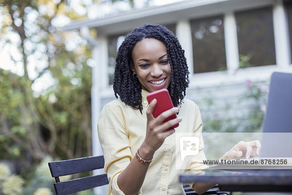 Smiling woman using cell phone and laptop on patio