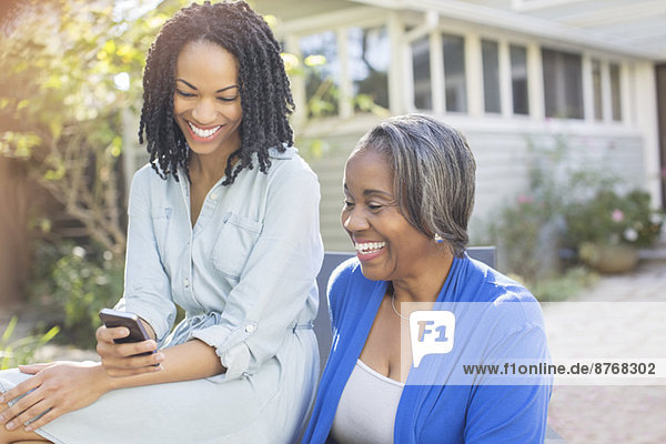 Lächelnde Mutter und Tochter SMS mit Handy auf der Terrasse
