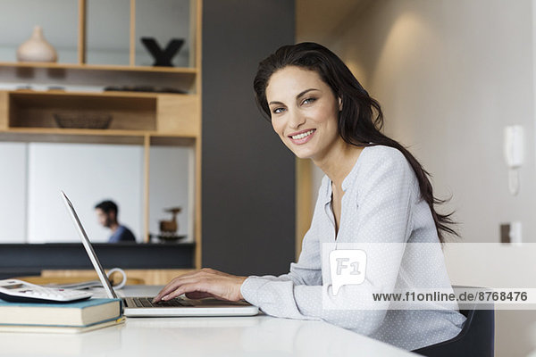 Porträt einer lächelnden Frau mit Laptop am Tisch