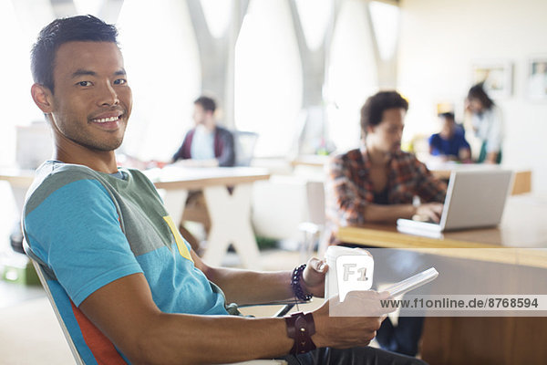 Porträt eines lächelnden Geschäftsmannes  der Kaffee trinkt und im Büro ein digitales Tablett benutzt.