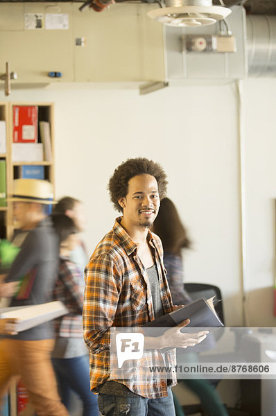 Porträt eines selbstbewussten Gelegenheitsunternehmers im Büro mit vorbeikommenden Mitarbeitern im Hintergrund