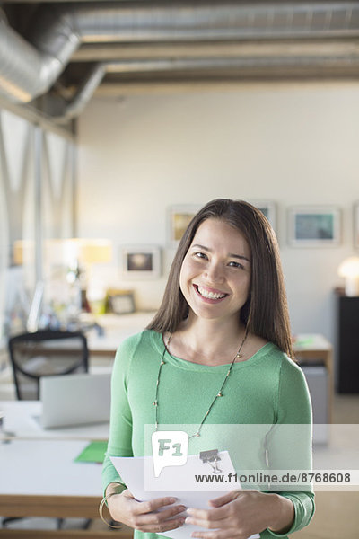 Porträt einer lächelnden Geschäftsfrau mit Papierkram im Amt