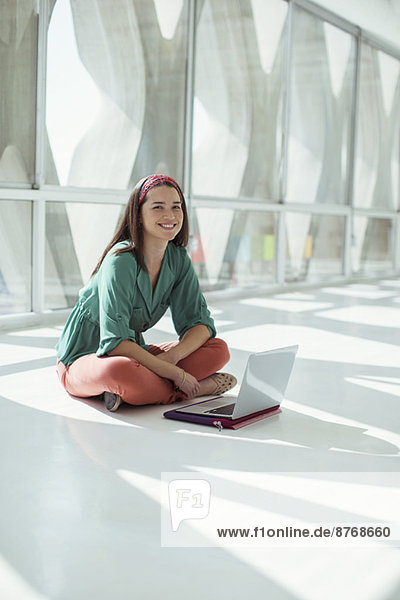Porträt einer selbstbewussten Geschäftsfrau mit Laptop auf dem Boden im sonnigen Büro