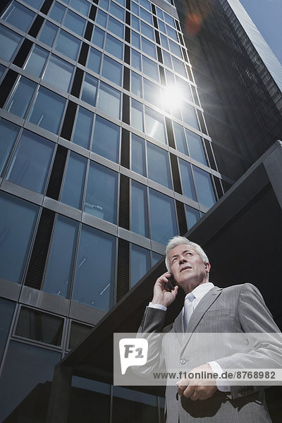 Senior Geschäftsmann am Handy vor dem Bürogebäude