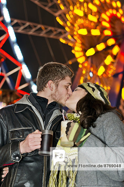 Deutschland  Berlin  glückliches junges Paar beim Küssen auf dem Weihnachtsmarkt vor dem beleuchteten Riesenrad