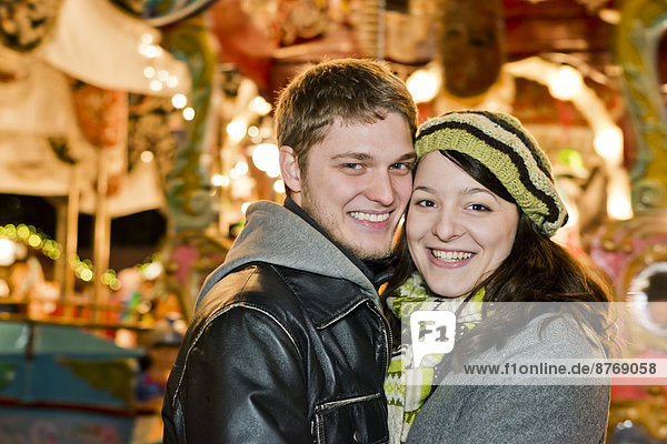Deutschland  Berlin  Porträt eines lächelnden jungen Paares Kopf an Kopf auf dem Weihnachtsmarkt