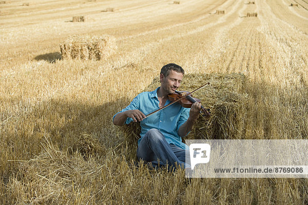 Man playing violin in stubble field