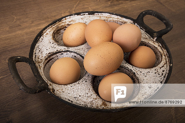 Frische braune Eier in alter Pfanne auf Holztisch