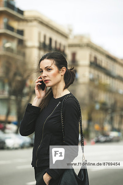 Spain  Catalunya  Barcelona  young black dressed businesswoman telephoning in front of a street
