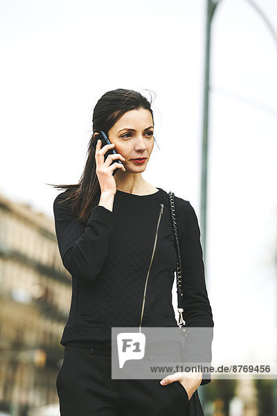 Spain  Catalunya  Barcelona  young black dressed businesswoman telephoning in front of a street