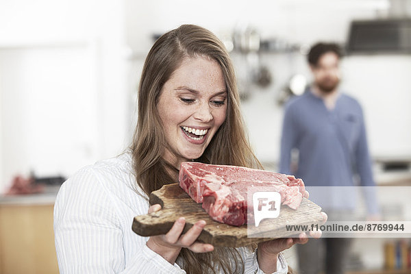 Happy young woman holding chopping board with raw steak