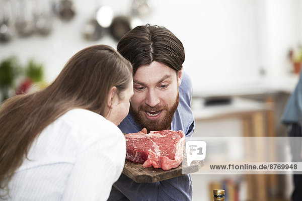 Man and woman in kitchen looking at steak