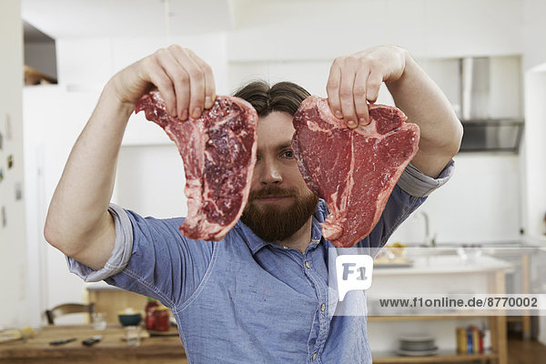Man in kitchen holding two steaks