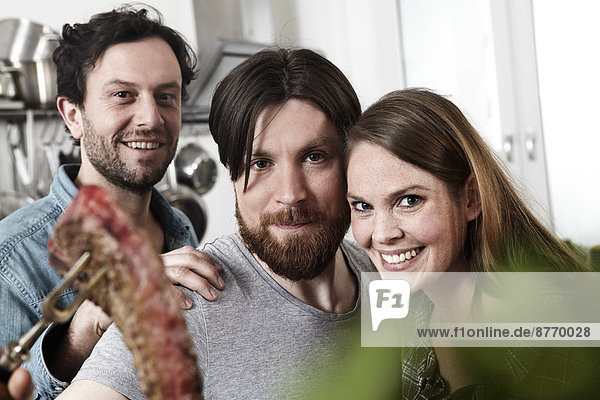 Portrait of three friends in kitchen with steak