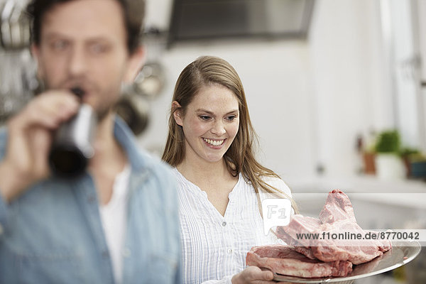 Man drinking beer and woman looking at raw steaks