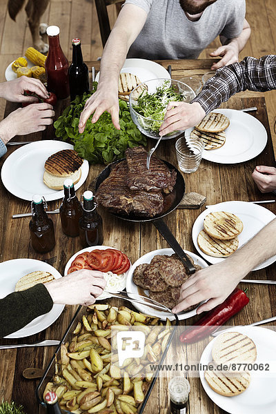 Freunde essen Kartoffeln  Steaks und Fleischbällchen an einem Holztisch.