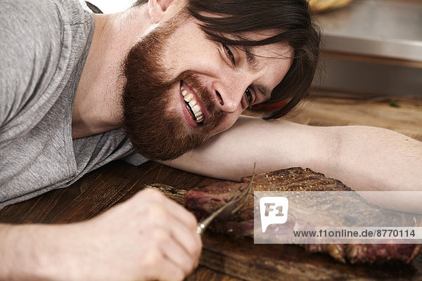 Happy man lying on table looking at large steak