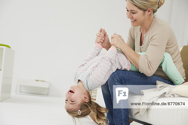 Deutschland  München  Mutter und Tochter auf dem Sofa sitzend  herumblödelnd
