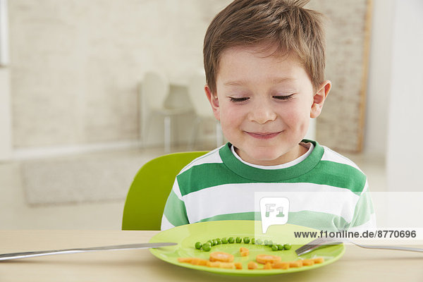 Junge isst Erbsen und Karotten mit anthropomorphem Gesicht.