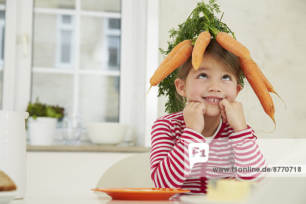 Mädchen am Tisch sitzend mit einem Haufen Karotten auf dem Kopf